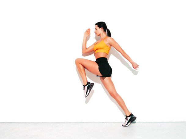 Fitness woman in sexy sports clothing. Young beautiful model with perfect body. Female posing in studio near white wall at summer sunny day. Jumping and running - Φωτογραφία, εικόνα