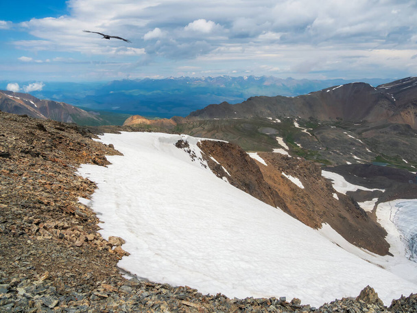 Φωτεινό αλπικό τοπίο με παγετώνες βουνά κάτω από μπλε συννεφιασμένο ουρανό. Γραφικό ορεινό τοπίο σε ηλιόλουστο καιρό. Όμορφη ατμοσφαιρική θέα από πέτρινο λόφο με χιόνι σε χιονισμένη οροσειρά. - Φωτογραφία, εικόνα