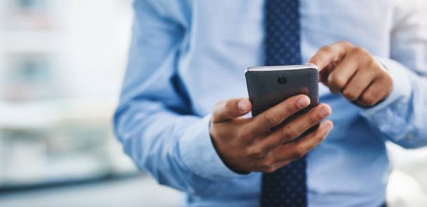 Taking a quick look at my social media. Cropped shot of an unrecognizable businessman standing alone in the office and using his cellphone to text. - Foto, imagen