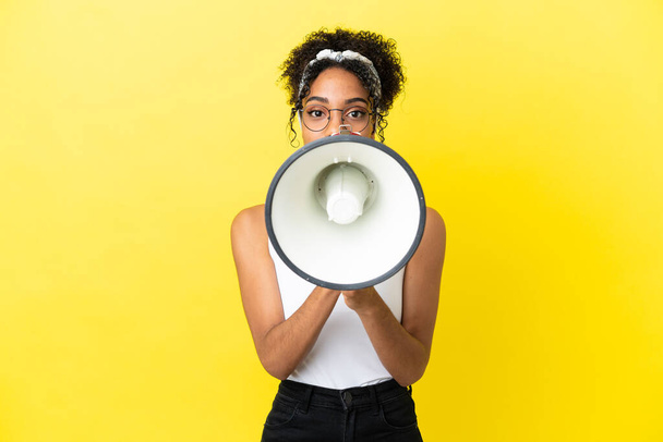Jeune femme afro-américaine isolée sur fond jaune criant à travers un mégaphone pour annoncer quelque chose - Photo, image