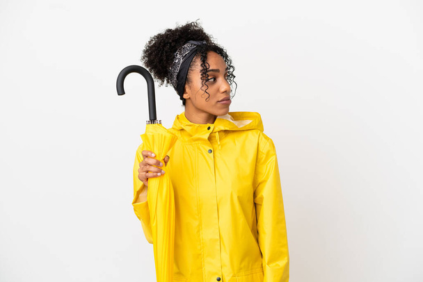 Young woman with rainproof coat and umbrella isolated on white background looking to the side - Photo, Image