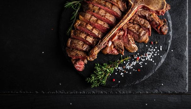Barbecue dry aged wagyu porterhouse beef steak sliced with large fillet piece with hot chili as closeup on a modern design black cast iron tray. - Zdjęcie, obraz