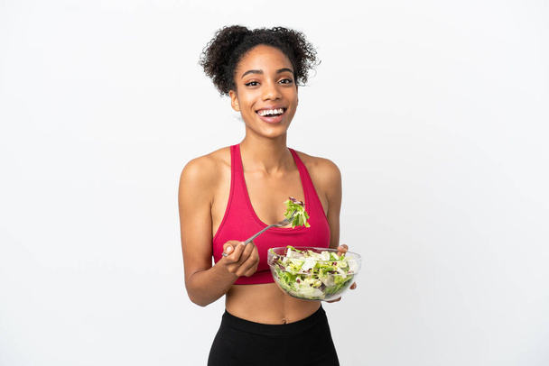 Junge afrikanisch-amerikanische Frau mit Salat isoliert auf weißem Hintergrund hält eine Schüssel Salat mit glücklichem Gesichtsausdruck - Foto, Bild