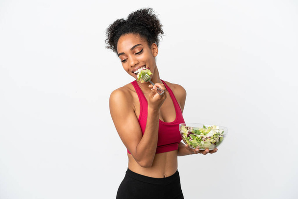 Молода афроамериканська жінка з салатом на білому тлі тримає миску салату і дивиться на неї з радісним виразом. - Фото, зображення