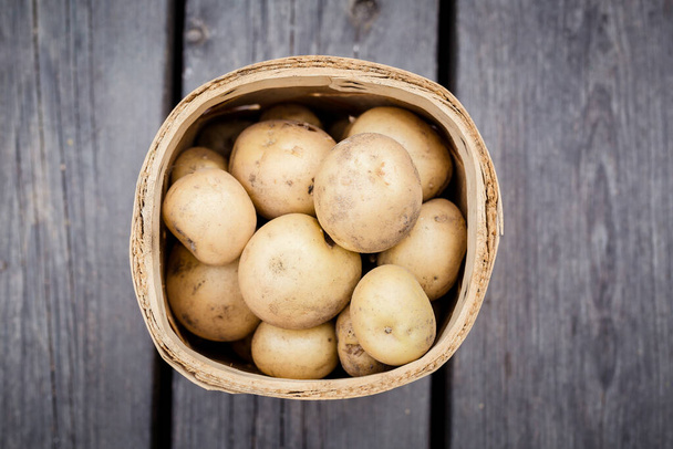 verse aardappelen in een houten doos op een rustieke achtergrond - Foto, afbeelding