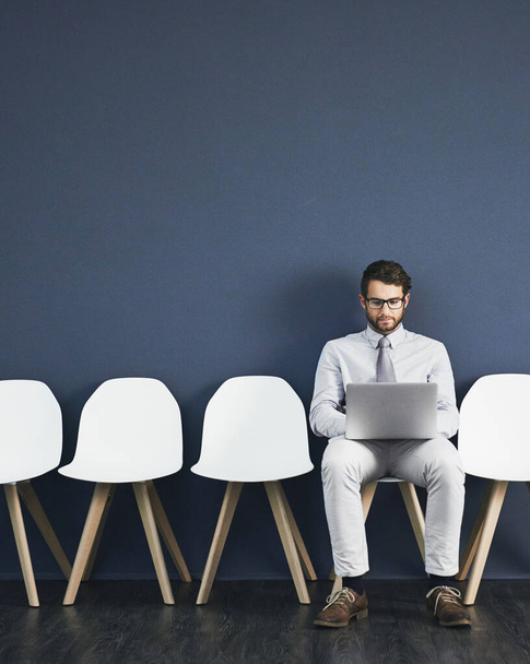 Минулої хвилини дослідження перед інтерв'ю. Студійний знімок молодого бізнесмена, який використовує ноутбук, чекаючи в черзі на сірому фоні
. - Фото, зображення