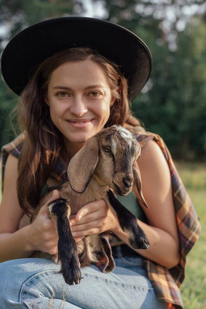 Beautiful woman farmer with small goat in countryside have friendship in nature - Photo, image