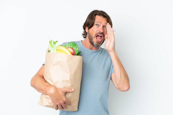 シニアオランダ人保持食料品ショッピングバッグ上の隔離された背景叫びとともに口全体オープン - 写真・画像