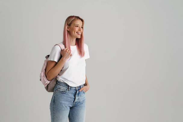 Усміхнена молода жінка стоїть з рюкзаком на сірому фоні
 - Фото, зображення
