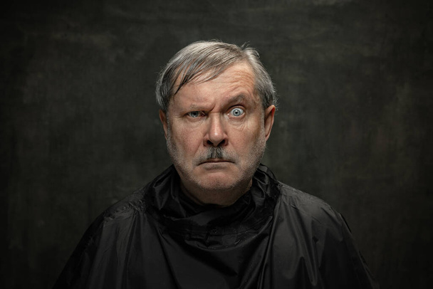 Portrait of angry senior man looking at camera isolated on dark vintage background. Concept of emotions, fashion, beauty, self-reinvention - Foto, immagini