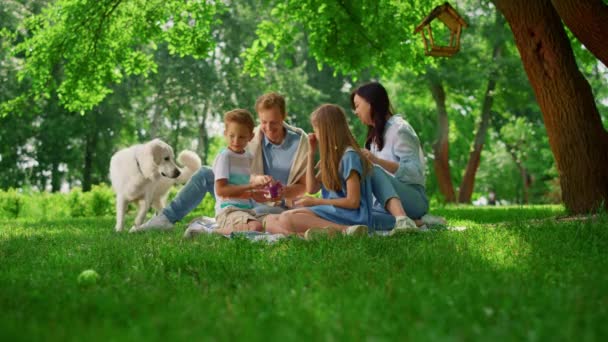 Gelukkige familie voeden witte hond op weekend picknick. Mensen rusten met huisdier in het park. - Video