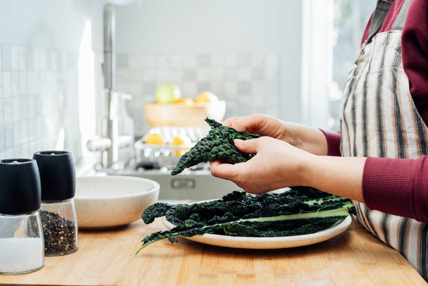 Woman tearing curly green kale leaves into pieces for kale, chips or salad. Healthy eating cooking step, ready to prepare food. Selective focus, copy space. - Photo, Image