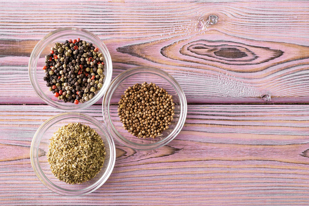Various spices in glass bowls on a purple wooden background. Black and red pepper, oregano, coriander. - Photo, Image