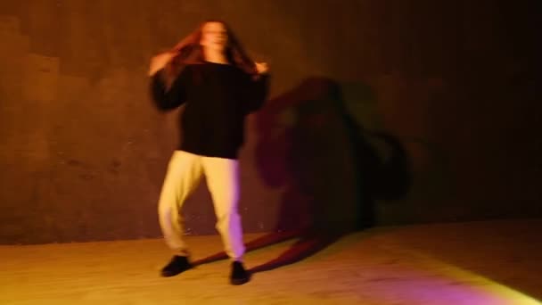 Choreografia tańca współczesnego. Zabawna młoda kobieta z długimi włosami tańczy hip hop, freestyle w sali tanecznej pod migającym jasnym światłem studyjnym. Strzał z punktu widzenia. - Materiał filmowy, wideo