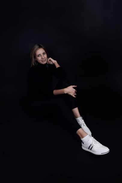 Young happy Caucasian woman with smile on her face with eyes looking at camera sitting on floor with black background. Time of good emotions. Good luck  - Foto, immagini