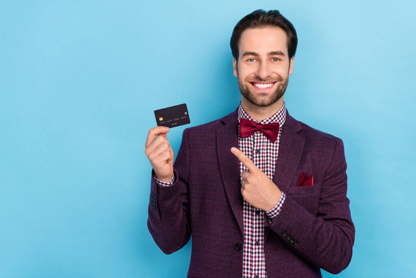 Foto di allegro uomo d'affari punta dito carta di credito promuovere banca carta di credito wireless isolato su sfondo di colore blu - Foto, immagini