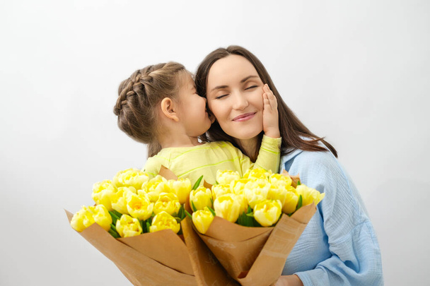 Концепция Дня матери, маленькая девочка и улыбающаяся мама с букетами цветов, желтыми тюльпанами, нежными объятиями, счастливым материнством - Фото, изображение