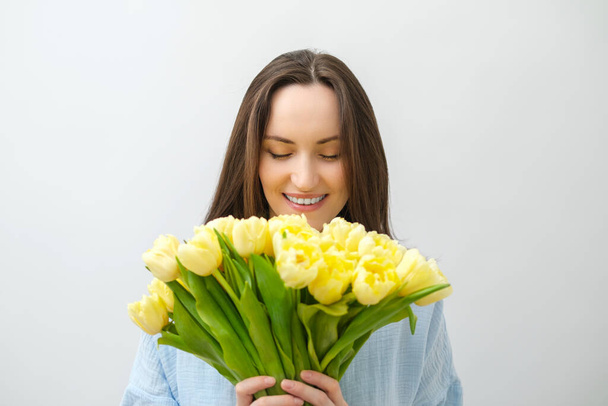 portrait of caucasian smiling brunette woman with yellow tulips with closed eyes, - Фото, зображення