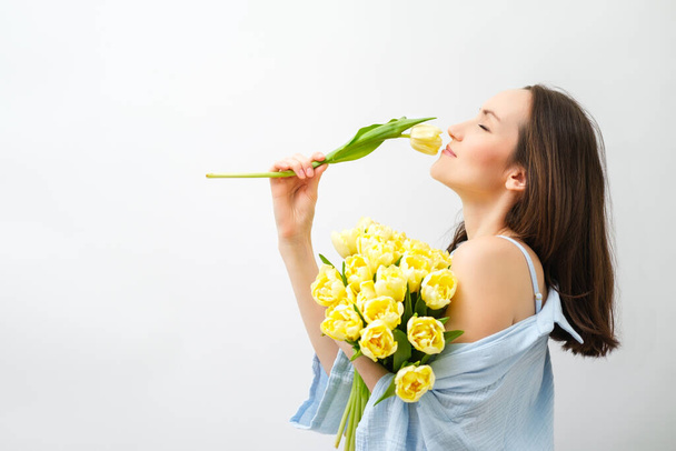 Biała brunetka kobieta w niebieskiej koszuli wdycha zapach żółtych tulipanów, koncepcja Dnia Matki, przestrzeń do kopiowania - Zdjęcie, obraz