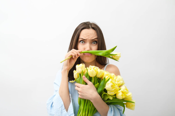 funny brunette beautiful woman in blue shirt with yellow tulips - 写真・画像