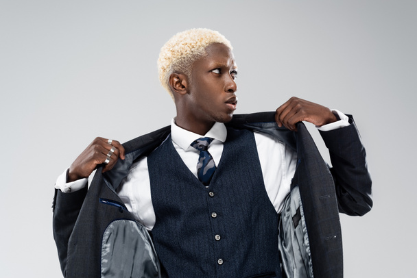 blonde african american man looking away and adjusting blazer isolated on grey  - Фото, зображення