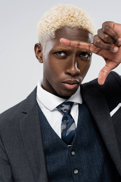 blonde african american businessman with blue eyes gesturing isolated on grey - 写真・画像