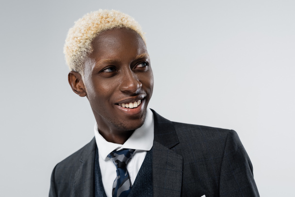 portrait of blonde african american man with blue eyes smiling isolated on grey  - Foto, afbeelding