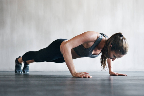 Ze tilt deze training naar een hoger niveau. Een foto van een vrouw die push-ups doet in de sportschool.. - Foto, afbeelding