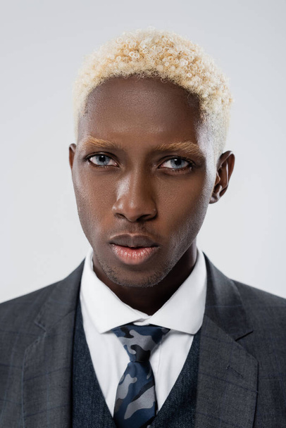 blondýny africký americký podnikatel s modrýma očima při pohledu na kameru izolované na šedé - Fotografie, Obrázek