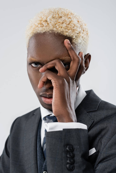 blonde african american businessman with blue eyes covering face and looking at camera isolated on grey - 写真・画像