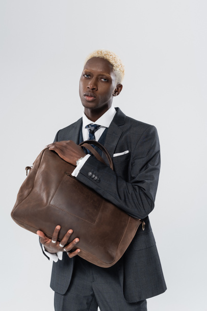 blonde african american man in suit holding leather bag isolated on grey  - Photo, Image