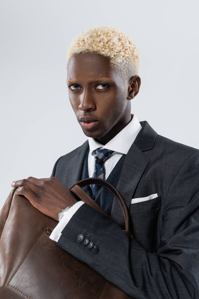 blonde african american man with blue eyes holding leather bag isolated on grey  - Foto, Imagem
