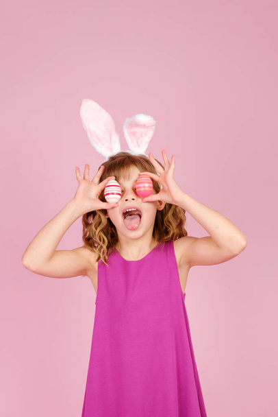 Delighted child covering eye with eggs during Easter party in pink studio - Fotó, kép