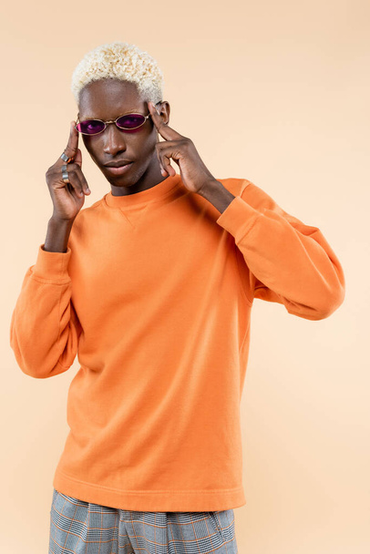mladý africký americký muž ve stylových slunečních brýlích a mikině izolované na béžové - Fotografie, Obrázek