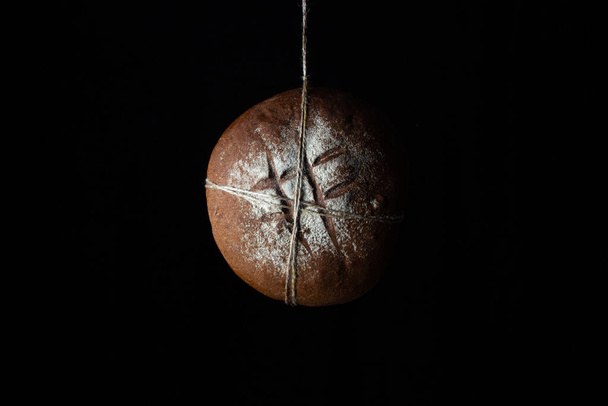 Brood op een zwarte achtergrond. Vers zelfgemaakt brood hangend aan een touw. Traditioneel voedsel - Foto, afbeelding