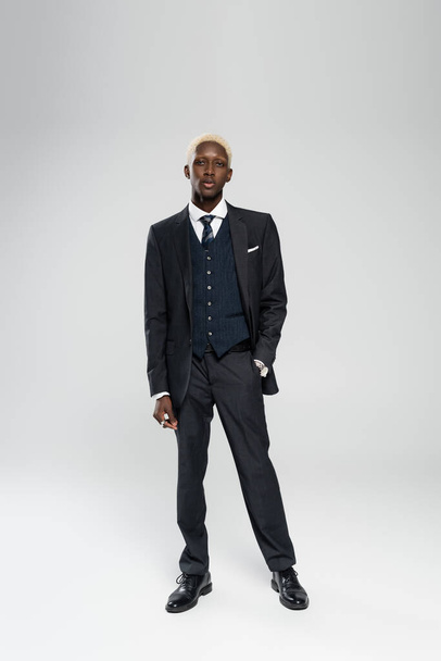full length of elegant african american man in formal wear standing with hand in pocket on grey - Foto, Imagem
