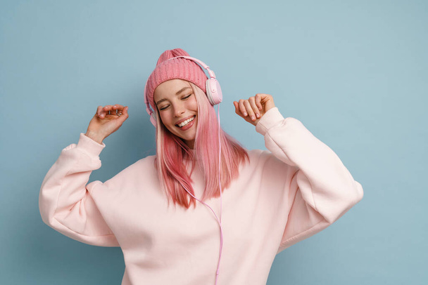 Young woman dancing while listening music with headphones isolated over blue wall - Fotoğraf, Görsel