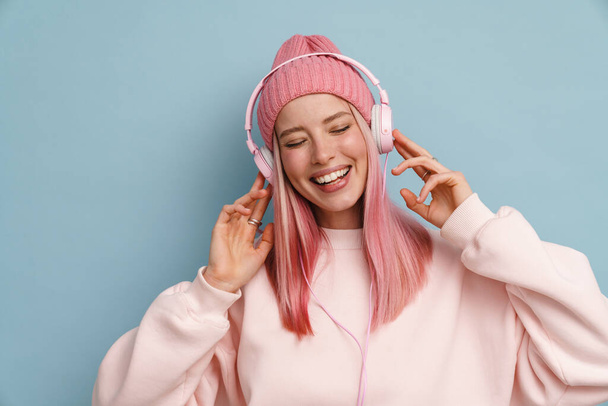 Young woman laughing while listening music with headphones isolated over blue wall - Φωτογραφία, εικόνα