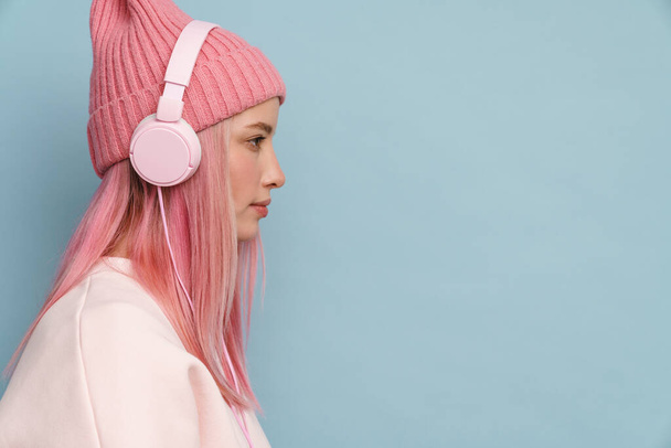 Young white woman wearing pink hat listening music with headphones isolated over blue wall - 写真・画像