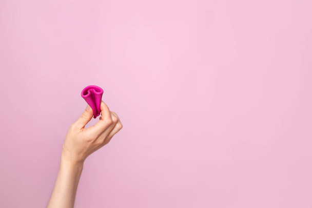 A young woman folding a pink menstrual cup in her hand. Pink colored background. Space for text. Eco-friendly silicone. women's health cycle High quality photo - 写真・画像