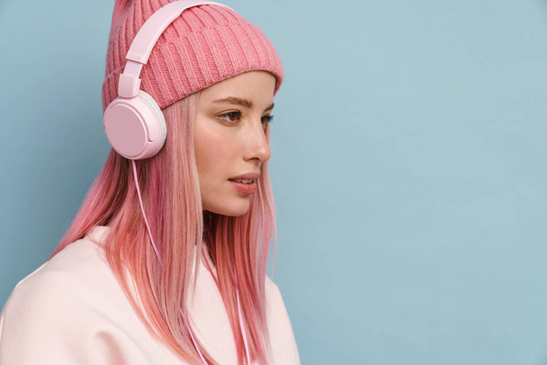 Young white woman wearing pink hat listening music with headphones isolated over blue wall - Фото, зображення