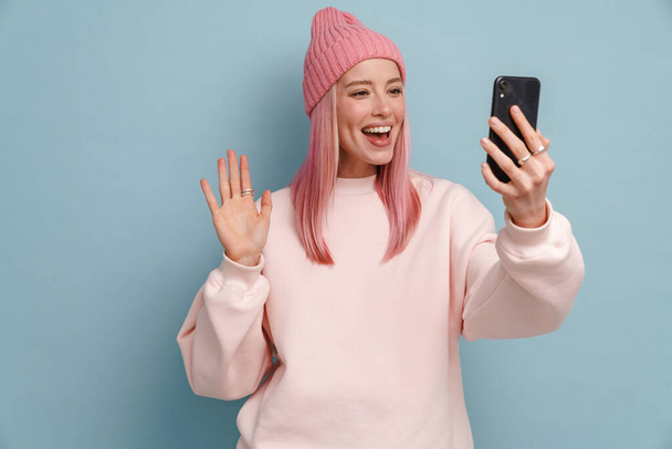 Young white woman gesturing while using mobile phone isolated over blue wall - Foto, Imagem