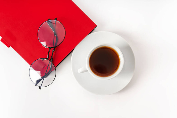 Ένα σύγχρονο γραφείο με ένα σημειωματάριο, ποτήρια και ένα φλιτζάνι καφέ ή τσάι σε λευκό φόντο με μια θέση για κείμενο - Φωτογραφία, εικόνα