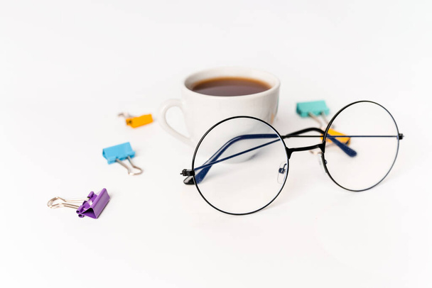 Egy bögre tea, szemüveg és elszórt színes gemkapocs fehér alapon. Irodai és üzleti koncepció - Fotó, kép