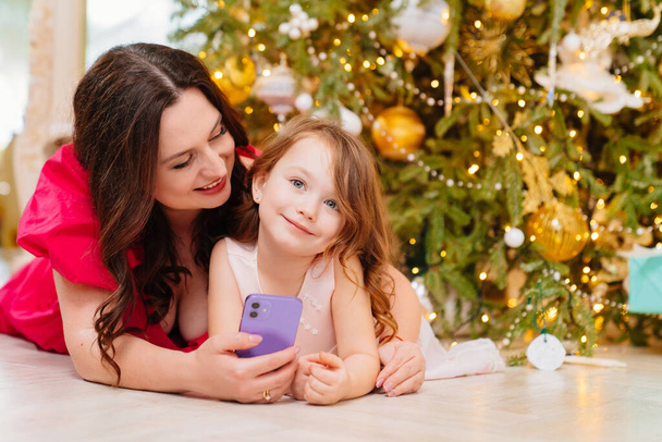 mother and daughter under the Christmas tree with a smartphone. - Foto, imagen