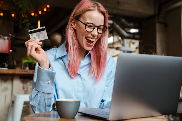 Young laughing woman using laptop and credit card while sitting in cafe - Φωτογραφία, εικόνα