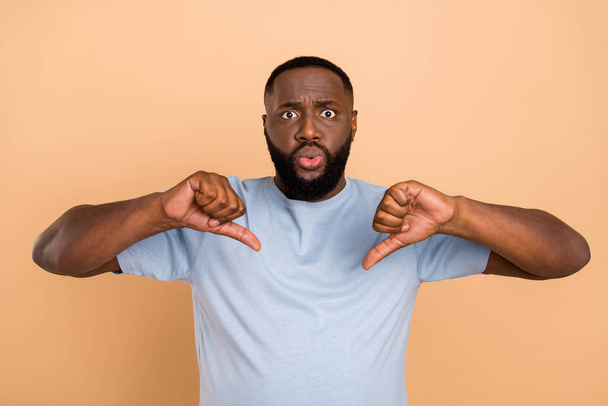 Photo of sad millennial beard guy show thumb down wear blue t-shirt isolated on beige color background - Φωτογραφία, εικόνα