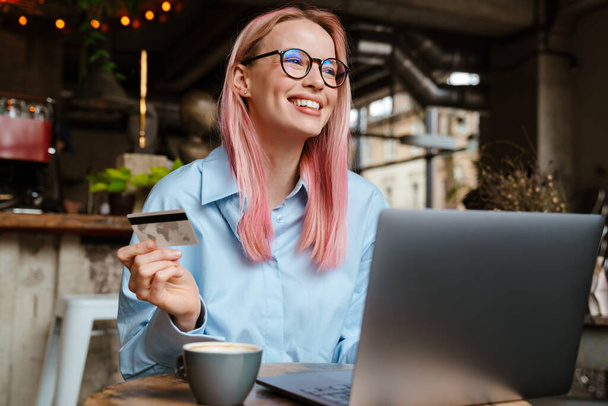 Young smiling woman using laptop and credit card while sitting in cafe - Foto, imagen