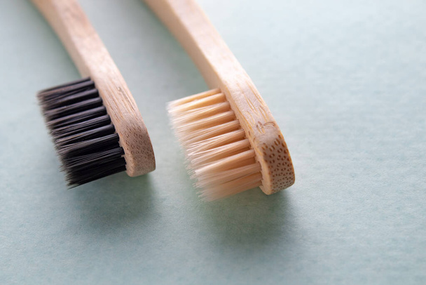 Two bamboo brushes with beige and black bristles on a green background. The concept of ecology and dental health. - Photo, Image