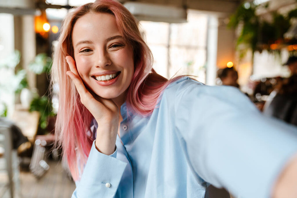 Young beautiful woman with pink hair smiling and taking selfie photo in cafe - Foto, imagen